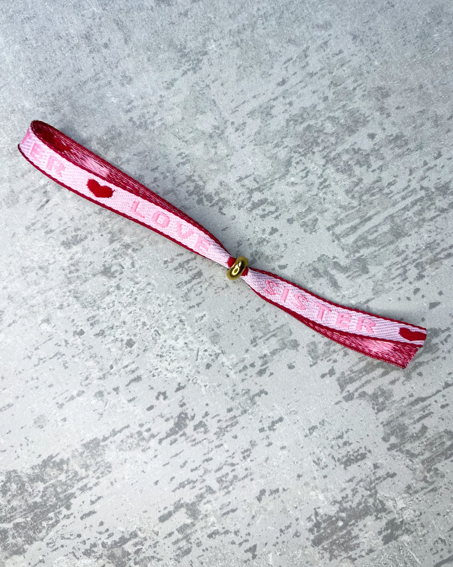 Dieses-Armband besteht aus sehr haltbarem Polyester und hat die Aufschrift "SISTER LOVE". Die goldfarbene Stopper-Perle ist aus rostfreiem Stahl.