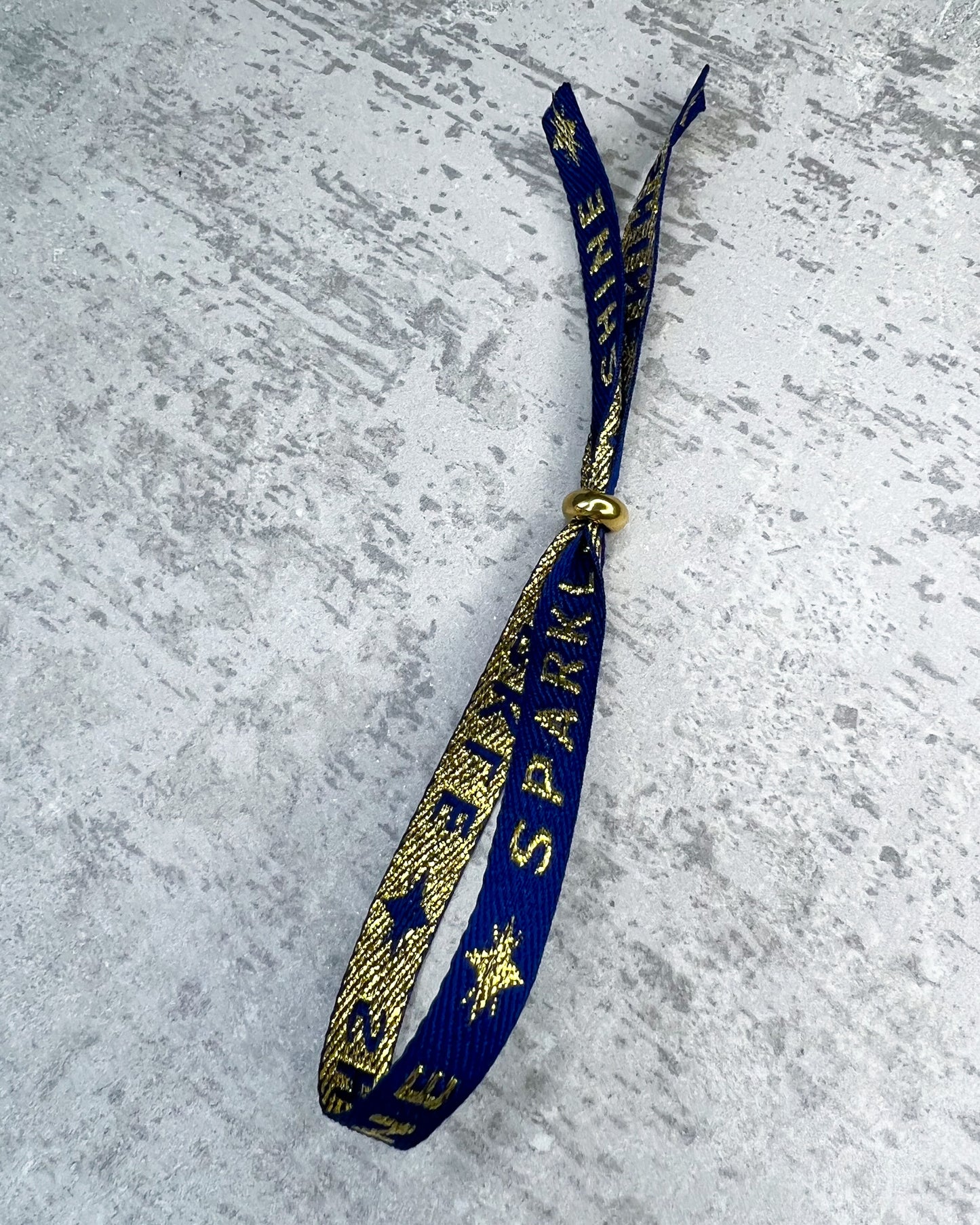Dieses-Armband besteht aus sehr haltbarem Polyester und hat die Aufschrift "SPARKLE & SHINE". Die goldfarbene Stopper-Perle ist aus rostfreiem Stahl.
