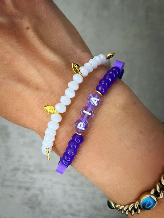 Doppeltes Heilstein-Armband mit wunderschönen, feinen und ausgesuchten Perlen. Dieses Armband ist handgearbeitet aus: facettierten, weißen Glasperlen, lilafarbenen, flachen lila gefärbten Jade-Perlen, goldfarbenen Blätter-Anhänger, lilafarbenen Polymer-Herzen, einer goldfarbenen Edelstahl-Perle & Buchstaben aus Acryl in lila transparent.