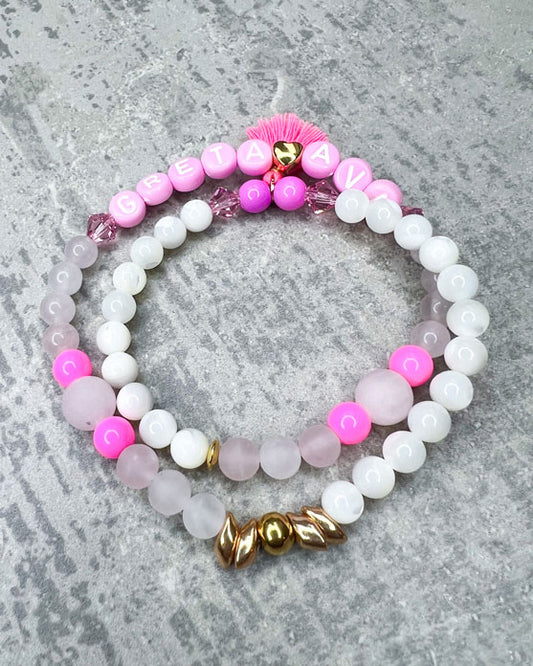 Heilstein-Armband mit wunderschönen, feinen und ausgesuchten Perlen. Dieses Armband ist handgearbeitet und doppelt gebunden aus: rosafarbenen Rosenquarz-Perlen, pink glitzernden Swarovski-Perlen, einem goldfarbenem Herz, pinken, goldenen und rosafarbenen Glasperlen, weißen Perlmutt-Perlen, einer neon-pinken Quaste, einer goldfarbenen Edelstahl-Perle & Buchstaben aus Acryl in rosa.