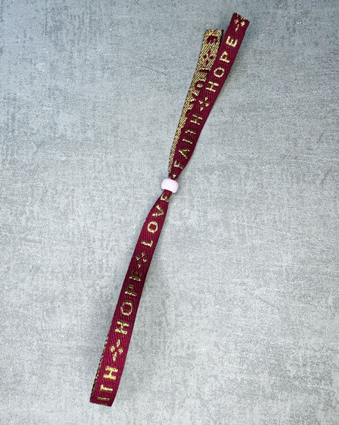 Dieses-Armband besteht aus sehr haltbarem Polyester und hat die Aufschrift "FAITH HOPE LOVE". Die goldfarbene Stopper-Perle ist aus rostfreiem Stahl.