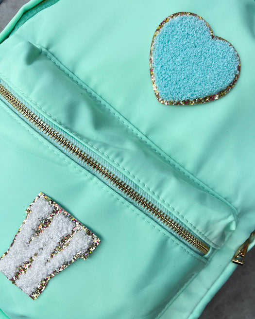 Der Nylonrucksack ist das It Piece unter unseren personalisierbaren Taschen. perfekt für Laptop, Ordner, Hefte und Co. geeignet, mit einer Innentasche sowie auf beiden Aussenseiten mit Taschen Die Schultergurte sind weich gepolstert und machen den Rucksack so auch für schwerere Inhalte. Das Aussenmaterial, Nylon, ist ausserdem wasserabweisend. Zum Personalisieren mit süßen Glitzer-Buchstaben-Patches, Smileys oder Herzen.