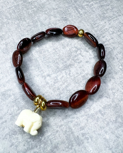 Tigerauge-Armband aus wunderschönen, feinen und ausgesuchten Perlen! Dieses Armband ist handgearbeitet aus: rot/braunen Tigeraugen-Edelsteinen, goldfarbenen Spacer-Perlen, einer goldfarbenen Edelstahlkugel & einem Acryl-Anhänger in Form eines Elefanten.