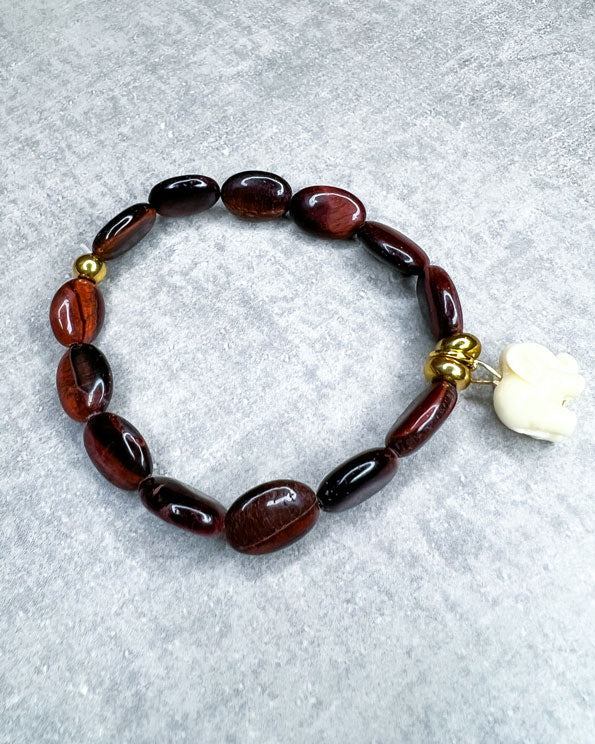 Tigerauge-Armband aus wunderschönen, feinen und ausgesuchten Perlen! Dieses Armband ist handgearbeitet aus: rot/braunen Tigeraugen-Edelsteinen, goldfarbenen Spacer-Perlen, einer goldfarbenen Edelstahlkugel & einem Acryl-Anhänger in Form eines Elefanten.