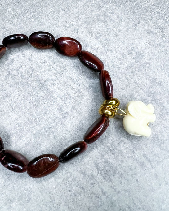 Tigerauge-Armband aus wunderschönen, feinen und ausgesuchten Perlen! Dieses Armband ist handgearbeitet aus: rot/braunen Tigeraugen-Edelsteinen, goldfarbenen Spacer-Perlen, einer goldfarbenen Edelstahlkugel & einem Acryl-Anhänger in Form eines Elefanten.