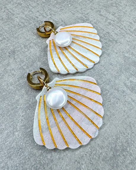 Dieser Ohrring ist gefertigt aus einer goldenen Edelstahl-Creole, einem weiß glitzernden Muschel-Anhänger aus Acryl und einem flach-runden Perlen-Anhänger.