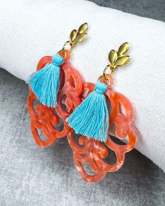 Dieser Ohrring ist gemacht mit: einem Ohrstecker aus rostfreiem Stahl in "Lilien-Optik", einem Ornament-Anhänger in der Farbe "Coral" und einer großen türkisen Quaste.