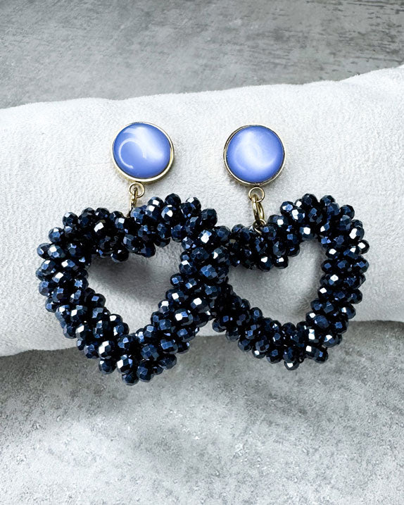 Dieser Ohrring ist gefertigt aus einem Cabochon-Stecker mit einem hellblau, glänzenden Stein und einem glitzernden Facetten-Herz-Anhänger in der Farbe "Silver Black.