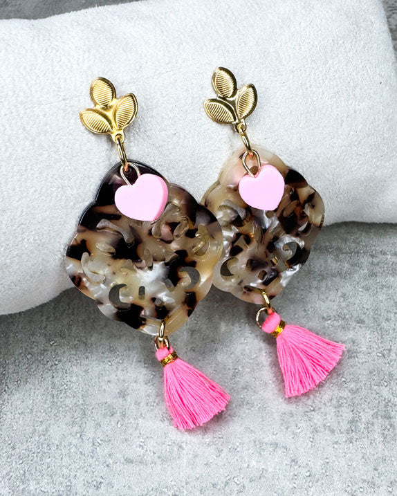 Dieser Ohrring ist gefertigt aus einem blütenförmigen Ohrstecker aus rostfreiem Stahl, einem Ornament-Anhänger in Schildpatt-Optik, einem rosafarbenem Polymer-Herz und einer Quaste in Neon-Rosa.