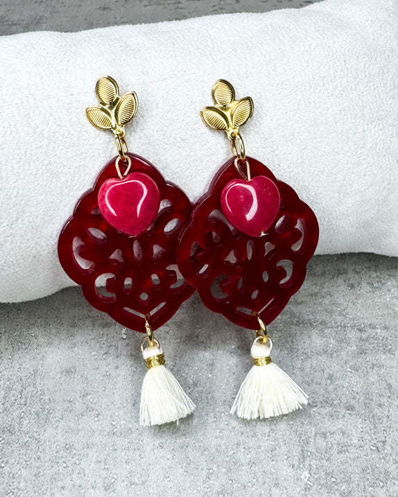 Dieser Ohrring ist gefertigt aus einem blütenförmigen Ohrstecker aus rostfreiem Stahl, einem Ornament-Anhänger in Rot, einem rot gefärbten Jade-Herz und einer Quaste in Creme.
