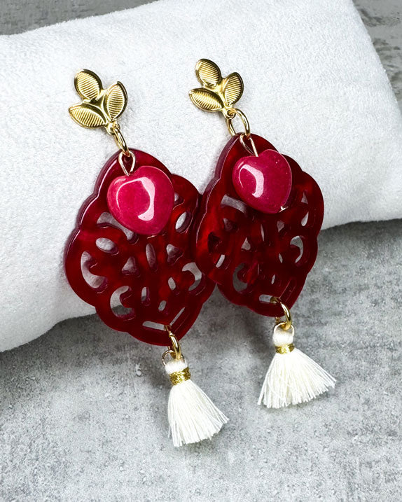 Dieser Ohrring ist gefertigt aus einem blütenförmigen Ohrstecker aus rostfreiem Stahl, einem Ornament-Anhänger in Rot, einem rot gefärbten Jade-Herz und einer Quaste in Creme.
