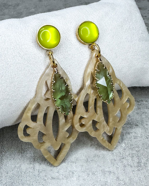 Dieser Ohrring ist gemacht mit:
einem goldfarbener "Polaris Steel" Ohrstecker mit einem gelb glänzenden Cabochon Stein, einem Ornament-Anhänger in der Farbe "Beige-Gold" und einem goldgefassten, grün facettierten Glas-Anhänger.