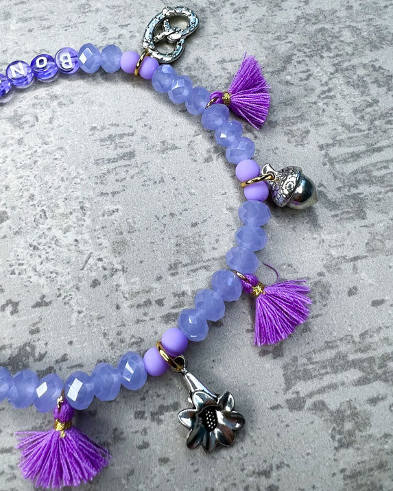 Von Hand gefertigter Schmuck für Dein Haustier.  Die Wiesn-Kette besteht aus lila glitzernden, facettierten Glasperlen, lilafarbenen Polymer, lila Acryl-Buchstabenperlen, lilafarbenen Quasten, silberfarbenen Wiesn-Anhängern, sowie einer goldfarbenen Edelstahlkugel. 
