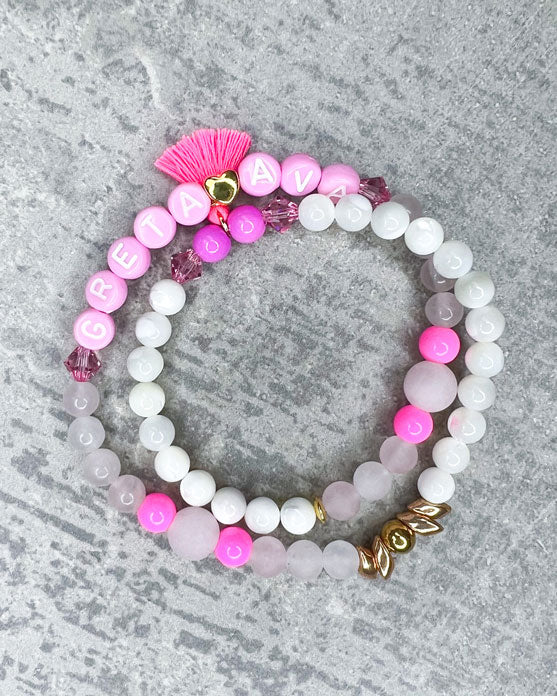 Heilstein-Armband mit wunderschönen, feinen und ausgesuchten Perlen.  Dieses Armband ist handgearbeitet und doppelt gebunden aus: rosafarbenen Rosenquarz-Perlen, pink glitzernden Swarovski-Perlen, einem goldfarbenem Herz, pinken, goldenen und rosafarbenen Glasperlen, weißen Perlmutt-Perlen, einer neon-pinken Quaste, einer goldfarbenen Edelstahl-Perle & Buchstaben aus Acryl in rosa.