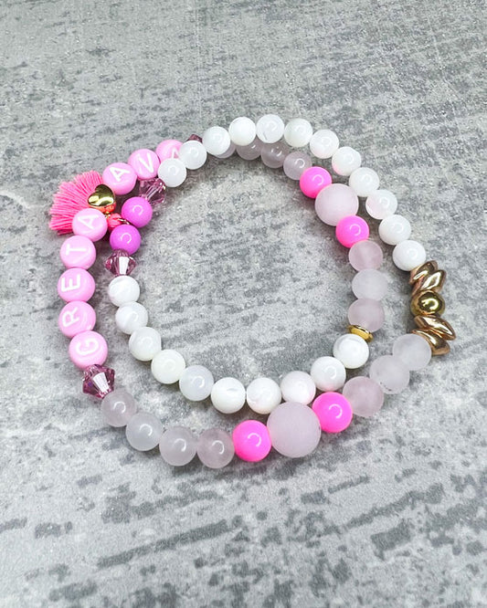 Heilstein-Armband mit wunderschönen, feinen und ausgesuchten Perlen.  Dieses Armband ist handgearbeitet und doppelt gebunden aus: rosafarbenen Rosenquarz-Perlen, pink glitzernden Swarovski-Perlen, einem goldfarbenem Herz, pinken, goldenen und rosafarbenen Glasperlen, weißen Perlmutt-Perlen, einer neon-pinken Quaste, einer goldfarbenen Edelstahl-Perle & Buchstaben aus Acryl in rosa.