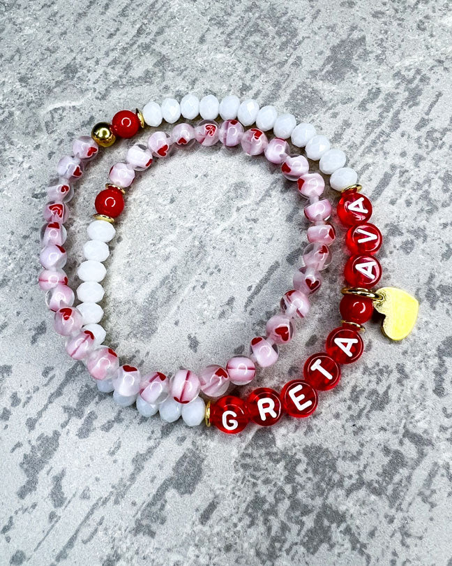 Doppeltes Armband mit wunderschönen, feinen und ausgesuchten Perlen.  Dieses Armband ist handgearbeitet aus: facettierten, weißen Glasperlen, Herzchen-Glasperlen, rote Glasperlen, einem Edelstahl-Herzanhänger, einer goldfarbenen Edelstahl-Perle & Buchstaben aus Acryl rot transparent.