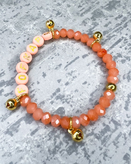 Handgemachtes Armband&nbsp;aus&nbsp;wunderschönen&nbsp;und ausgesuchten Perlen!  Dieses Armband ist handgearbeitet aus: pfirsich-farbenen, facettierten Glasperlen, goldfarbenen Metall-Glöckchen, pfirsich-farbenen Acryl-Buchstabenperlen und einer goldfarbenen Edelstahl-Verschlusskugel.
