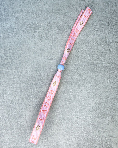 Dieses-Armband besteht aus sehr haltbarem Polyester und hat die Aufschrift "LIVE LAUGH LOVE". Die goldfarbene Stopper-Perle ist aus rostfreiem Stahl.