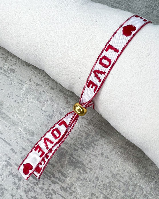 Dieses-Armband besteht aus sehr haltbarem Polyester und hat die Aufschrift "LOVE". Die goldfarbene Perle ist aus rostfreiem Stahl.