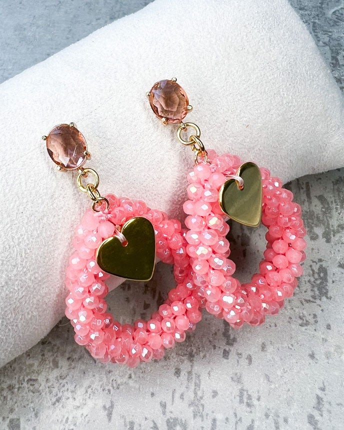 Ohrstecker mit einem pfirsichfarbenen, facettierten Glasstein, einem glitzernden Facetten-Perlen-Anhänger in der Farbe "Coral Pink" und einem goldfarbenem Herz-Anhänger.