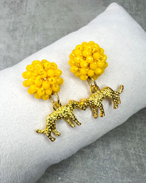Die Ohrringe bestehen aus: einem Ohrstecker mit fascettierten, gelben Glasperlen und einem grolfarbenem Leoparden als Anhänger.