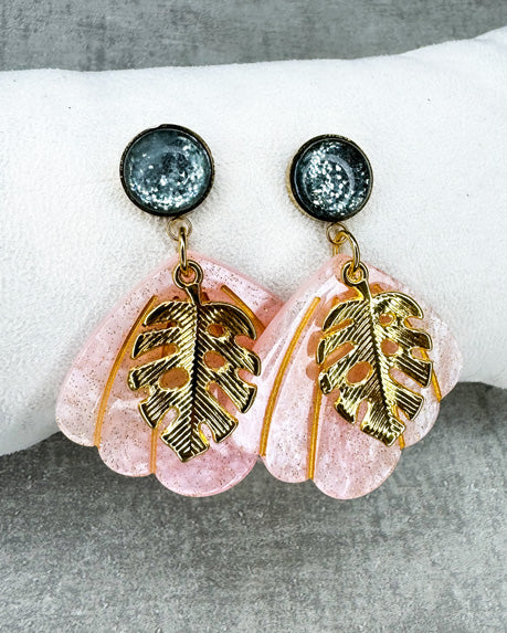 Dieser Ohrring ist gefertigt aus einem Cabochon-Ohrsstecker aus rostfreiem Stahl mit einem glänzenden, grün-glitzernden Cabochon-Stein, einem rosa glitzernden Muschel-Anhänger aus Acryl und einem goldfarbenem Blatt-Anhänger.