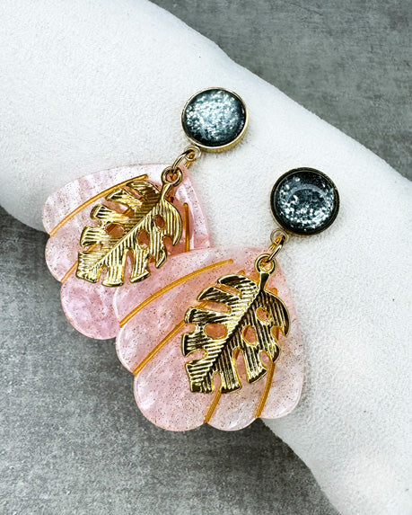 Dieser Ohrring ist gefertigt aus einem Cabochon-Ohrsstecker aus rostfreiem Stahl mit einem glänzenden, grün-glitzernden Cabochon-Stein, einem rosa glitzernden Muschel-Anhänger aus Acryl und einem goldfarbenem Blatt-Anhänger.