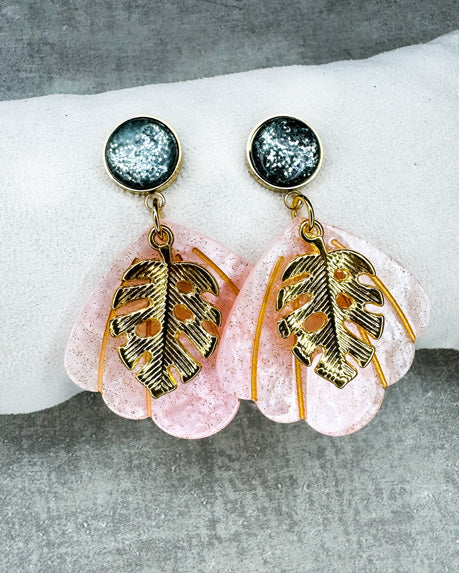 Dieser Ohrring ist gefertigt aus einem Cabochon-Ohrsstecker aus rostfreiem Stahl mit einem glänzenden, grün-glitzernden Cabochon-Stein, einem rosa glitzernden Muschel-Anhänger aus Acryl und einem goldfarbenem Blatt-Anhänger.