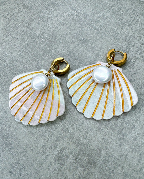 Dieser Ohrring ist gefertigt aus einer goldenen Edelstahl-Creole, einem weiß glitzernden Muschel-Anhänger aus Acryl und einem flach-runden Perlen-Anhänger.