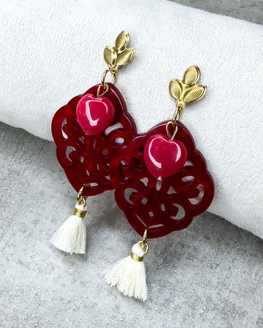 Dieser Ohrring ist gefertigt aus einem blütenförmigen Ohrstecker aus rostfreiem Stahl, einem Ornament-Anhänger in Rot, einem rot gefärbten Jade-Herz und einer Quaste in Creme.