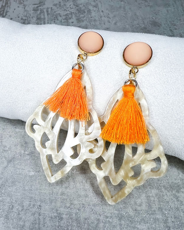 Dieser Ohrring ist gemacht mit: einem goldfarbener "Polaris Steel" Ohrstecker mit einem orange, matten Cabochon Stein, einem Ornament-Anhänger in der Farbe "Beige-Gold" und einer großen orangefarbenen Quaste.