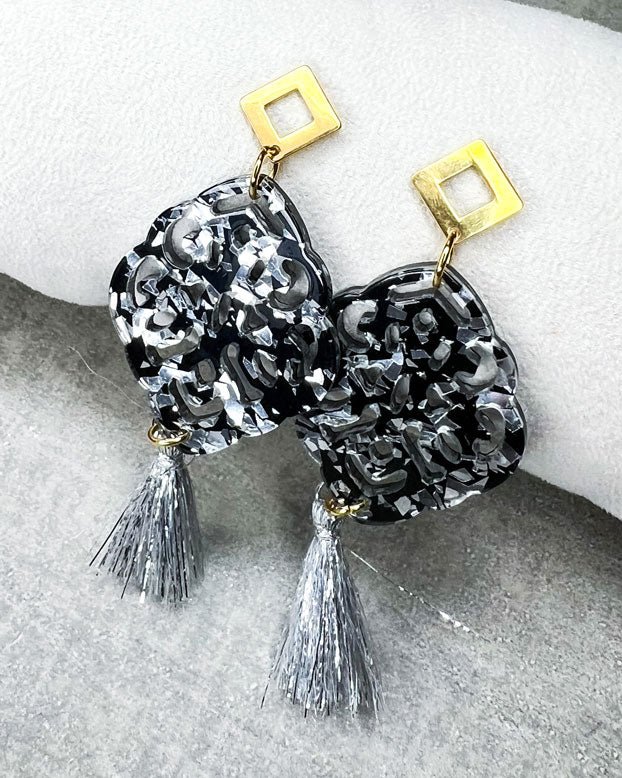Rautenförmiger Ohrstecker aus rostfreiem Stahl mit einem Ornament-Anhänger in der Farbe "Silver-Black" und einer silberfarbenen Quaste.