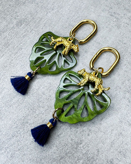 Dieser Ohrring ist gefertigt aus einer Creole aus rostfreiem Stahl mit weißen Zirkonia-Glitzersteinen vorne, einem Ornament-Anhänger in Green, einem goldfarbenen Panther als Anhänger und einer Quaste in Dunkelblau.