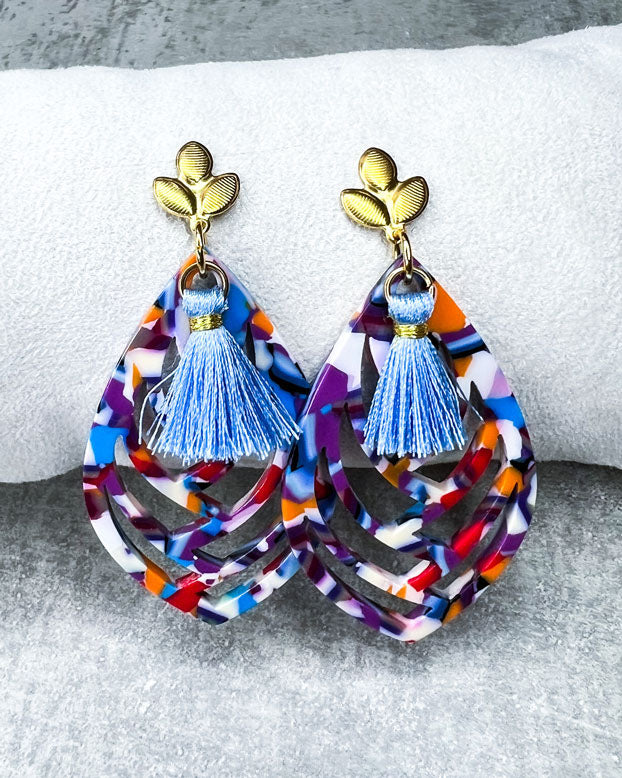 Diese Ohrringe sind gefertigt mit einem Ohrstecker aus rostfreiem Stahl in "Lilien-Form", mit einem bunten Ornament-Anhänger und einer hellblauen Quaste.