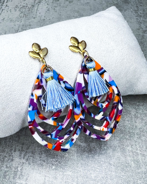 Diese Ohrringe sind gefertigt mit einem Ohrstecker aus rostfreiem Stahl in "Lilien-Form", mit einem bunten Ornament-Anhänger und einer hellblauen Quaste.