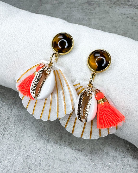 Dieser Ohrring ist gefertigt aus einem Polaris Steel Ohrstecker, einem Cabochon-Stein in Schildpatt-Optik, einem weiß glitzernden Muschel-Anhänger aus Acryl, einer gold verzierten Muschel als Anhänger und einer neon orangenen Quaste.
